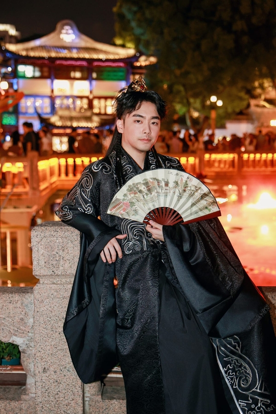Jonathan in a black traditional robe holding a folding fan at night in Shanghai